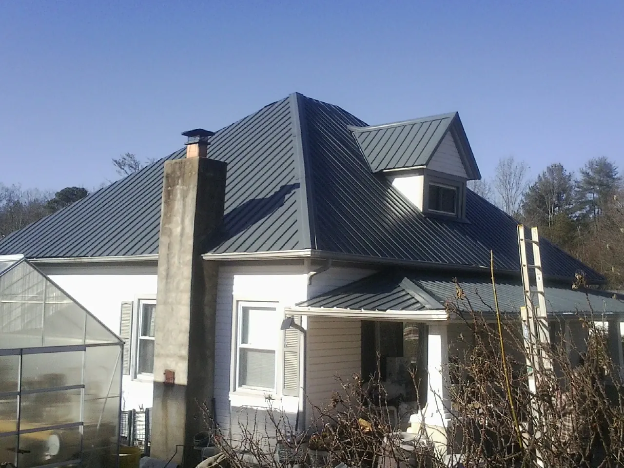 Dark blue standing seam metal roof on a white farmhouse with dormer — Slate & Tile Roof Repair by Roofing Brothers in Cathedral City