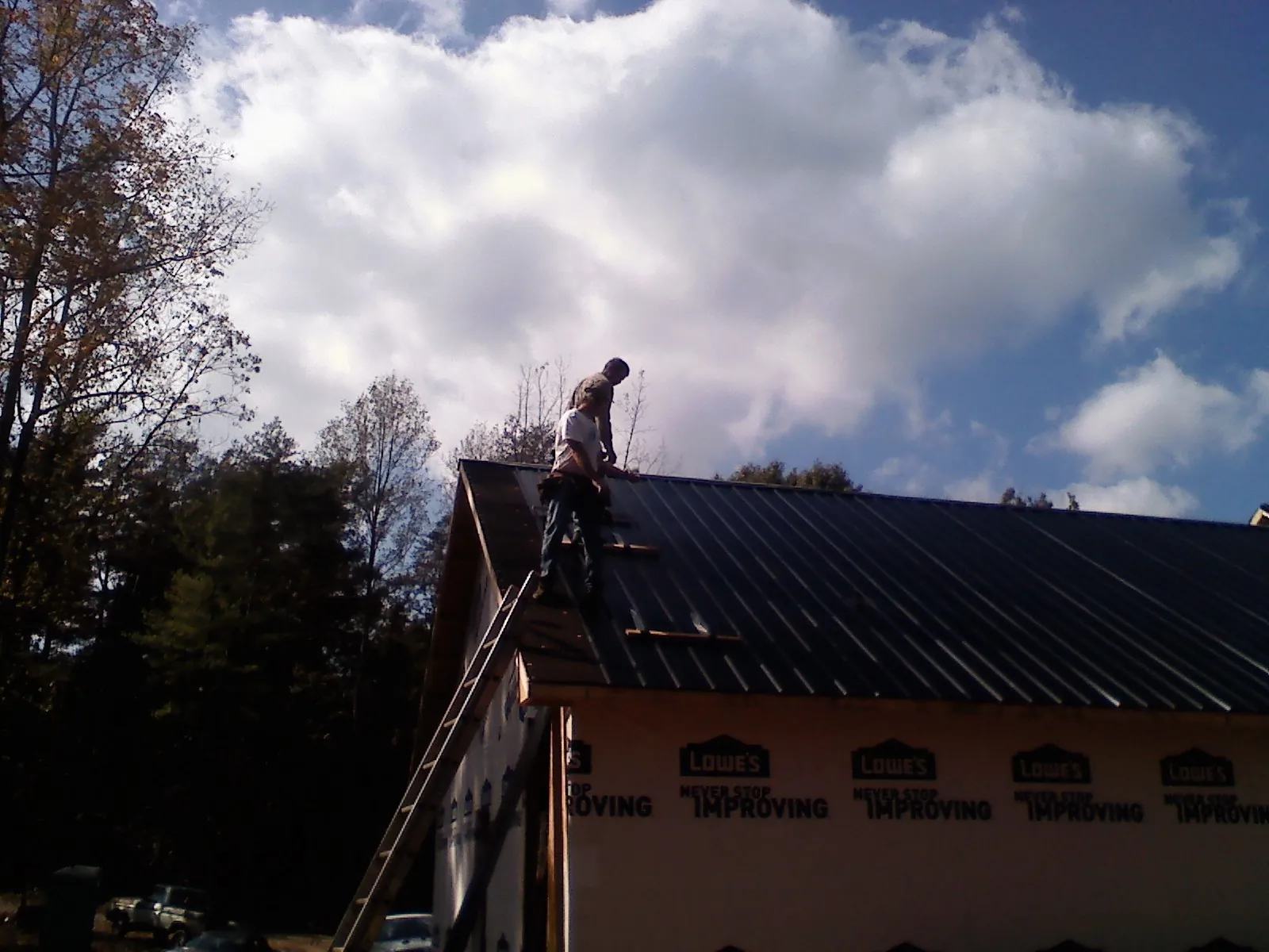 Roofer fastening dark metal panels high against a cloudy sky, from a Roof Inspection job in Cathedral City