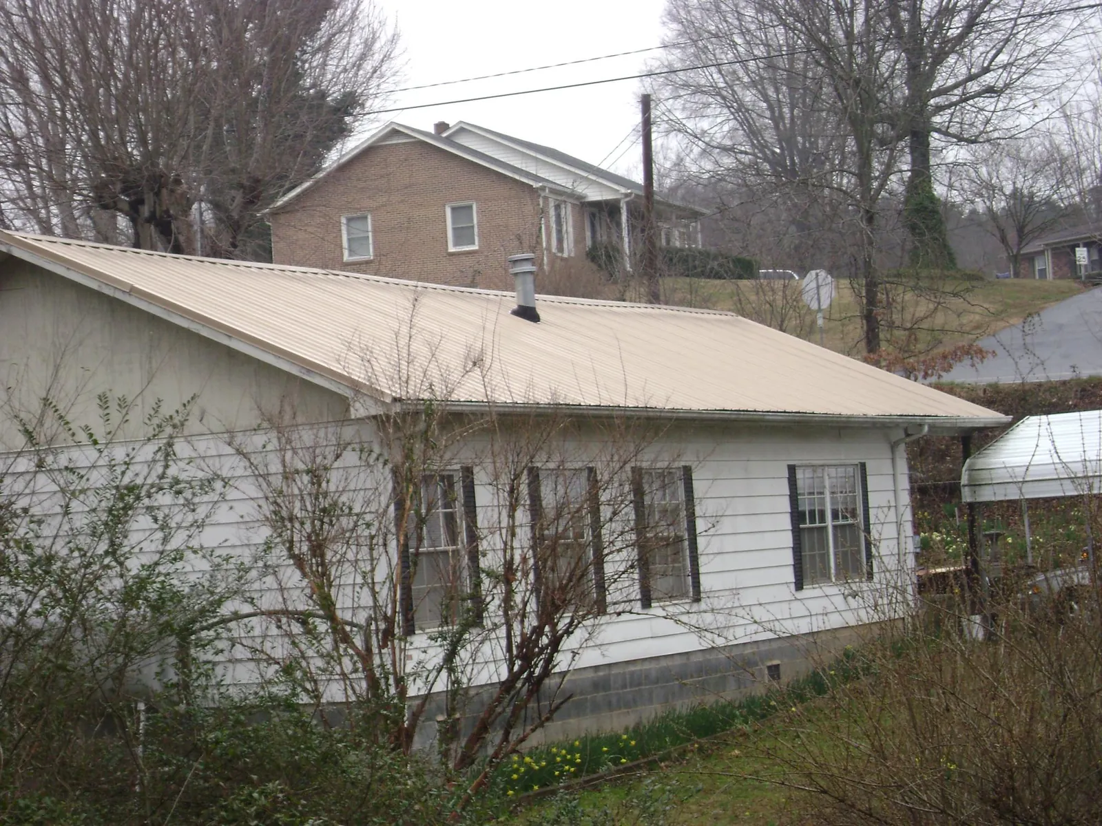 Tan metal roof on a white sided house set into a hillside — Commercial Roofing by Roofing Brothers in Cathedral City